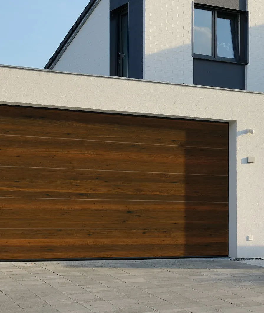 Garagentor in dunkler Nussbaum-Holzoptik an modernem Einfamilienhaus mit Pflastereinfahrt – Garagentore in Weyhausen von REIMANN